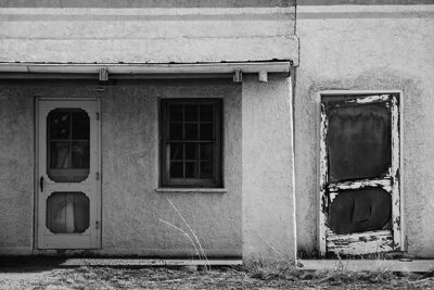 An image of an old vacated building in New Mexico (Fort Bayard near Silver City). Rich texture, simple planes and shapes, rendered in shades of grey. The building creates an image that takes one back in time and whispers stories of the past.